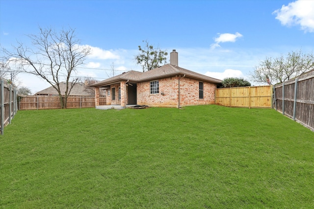 back of house with a yard, brick siding, a chimney, and a fenced backyard