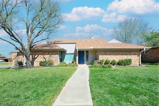 view of front of property featuring a shingled roof, a front yard, brick siding, and a chimney