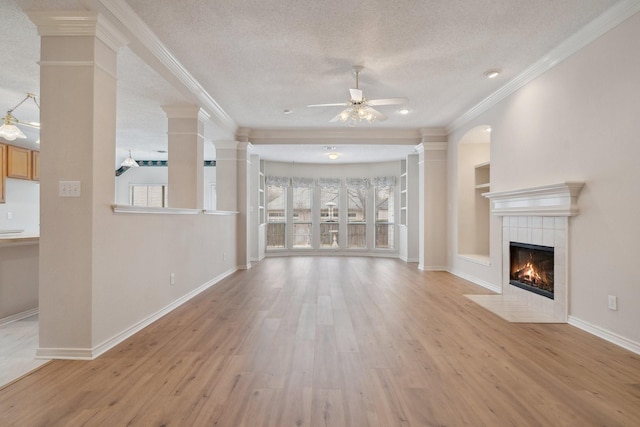 unfurnished living room featuring ornate columns, a tiled fireplace, light wood finished floors, and a textured ceiling