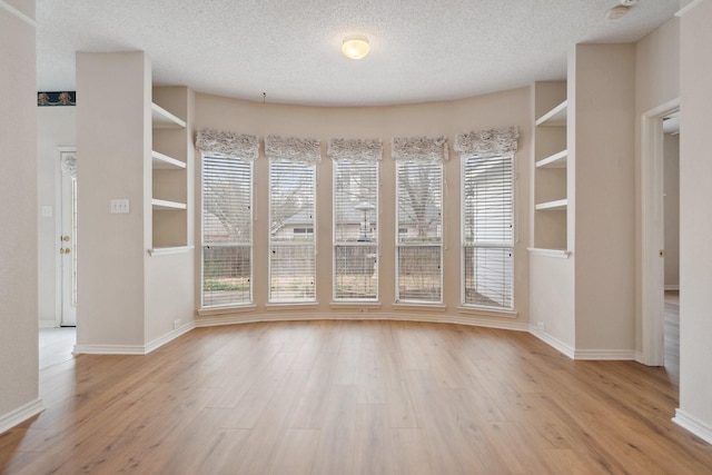 interior space with light wood-style floors, a wealth of natural light, a textured ceiling, and baseboards