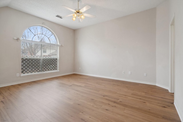 empty room featuring a textured ceiling, light wood-style flooring, visible vents, baseboards, and a ceiling fan