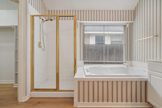 full bathroom featuring wallpapered walls, a stall shower, wood finished floors, a spacious closet, and a bath