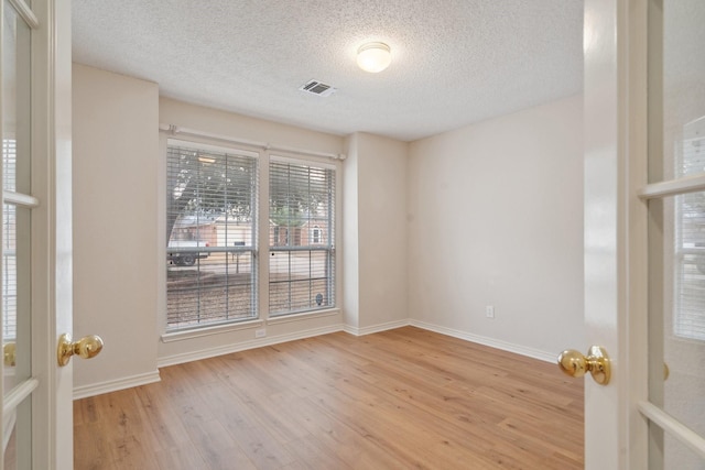 unfurnished room with baseboards, a textured ceiling, visible vents, and wood finished floors