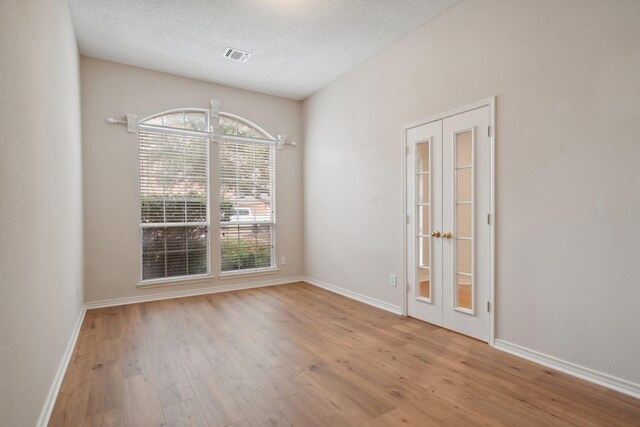 empty room featuring baseboards, visible vents, wood finished floors, a textured ceiling, and french doors