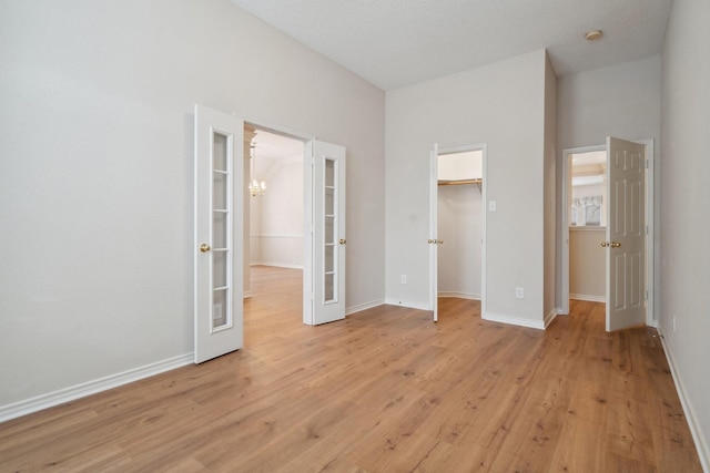 unfurnished bedroom with french doors, light wood-style flooring, baseboards, and a spacious closet