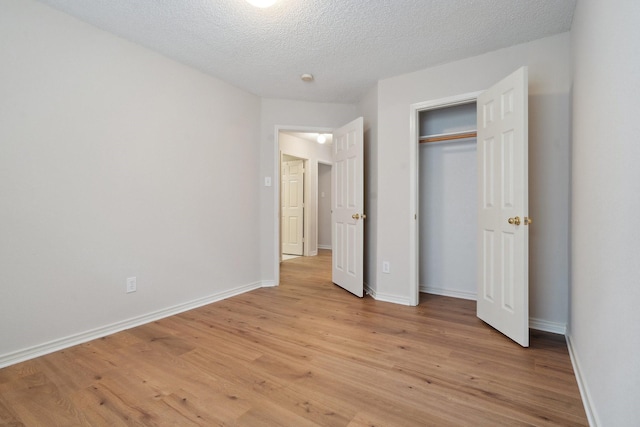 unfurnished bedroom featuring light wood-type flooring, a closet, baseboards, and a textured ceiling