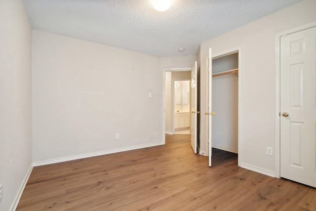 unfurnished bedroom featuring light wood-type flooring, a closet, a textured ceiling, and baseboards