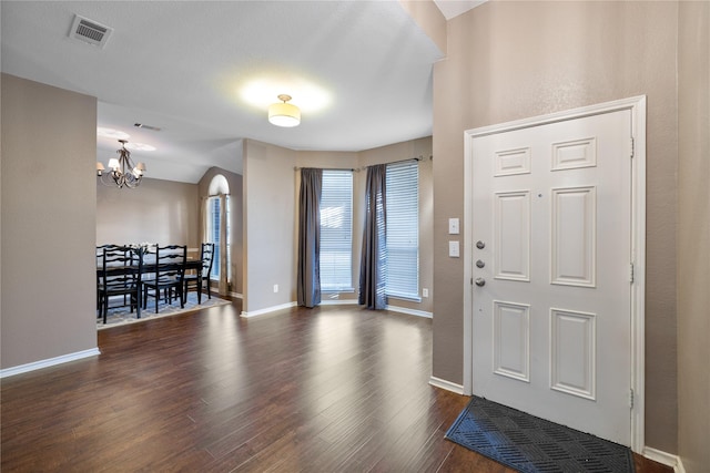 entryway featuring arched walkways, dark wood-type flooring, visible vents, baseboards, and an inviting chandelier