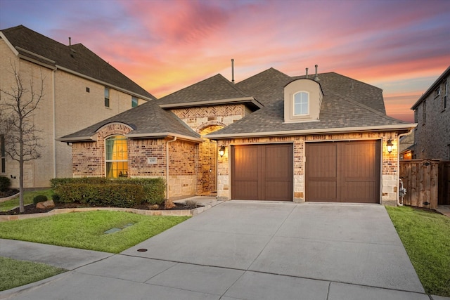 french country inspired facade featuring an attached garage, concrete driveway, brick siding, and a shingled roof