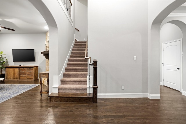 stairs with ceiling fan, baseboards, arched walkways, and wood finished floors