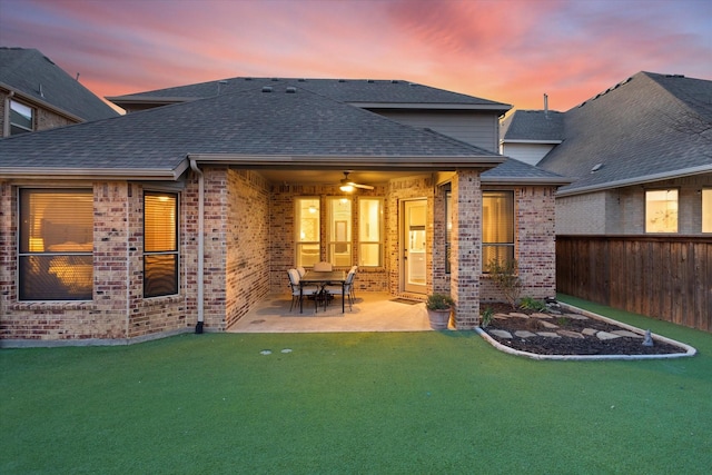 back of property at dusk featuring brick siding, a patio area, fence, and a shingled roof