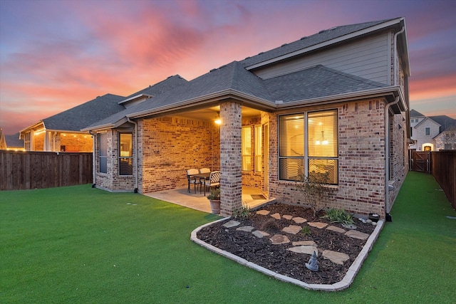 back of property with brick siding, a patio, a fenced backyard, and roof with shingles