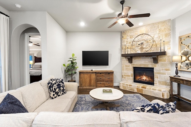 living area with arched walkways, recessed lighting, a ceiling fan, a stone fireplace, and wood finished floors