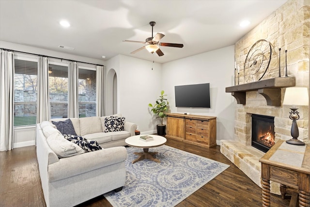 living area with visible vents, arched walkways, a ceiling fan, wood finished floors, and a stone fireplace