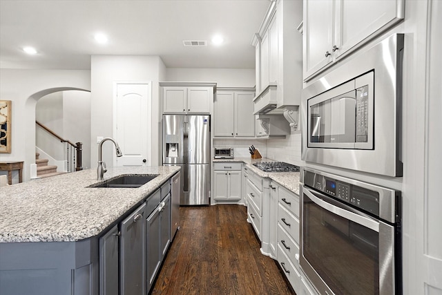 kitchen with light stone counters, stainless steel appliances, tasteful backsplash, visible vents, and a sink