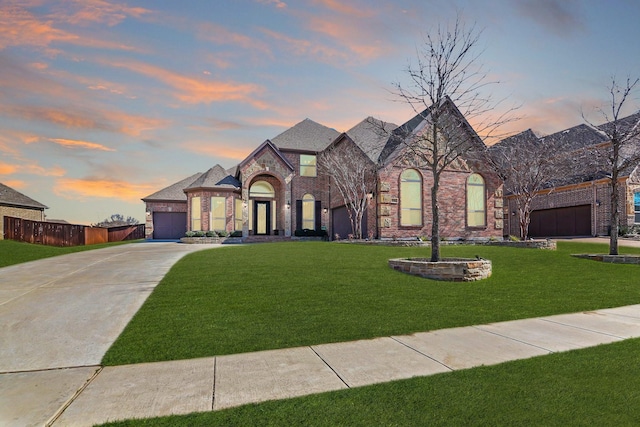 french country inspired facade with brick siding, a front lawn, fence, concrete driveway, and an attached garage