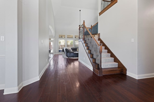 interior space featuring baseboards, a high ceiling, hardwood / wood-style floors, and arched walkways