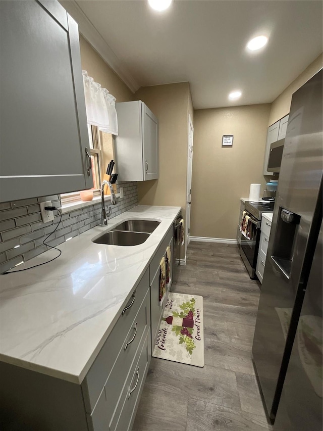 kitchen featuring gray cabinets, backsplash, appliances with stainless steel finishes, a sink, and light stone countertops