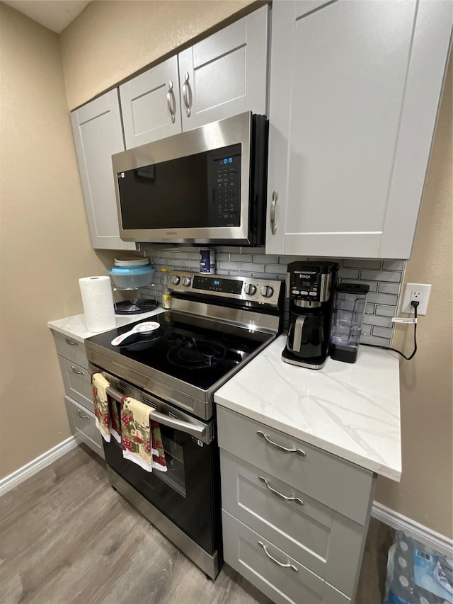 kitchen with light wood finished floors, appliances with stainless steel finishes, backsplash, and gray cabinetry