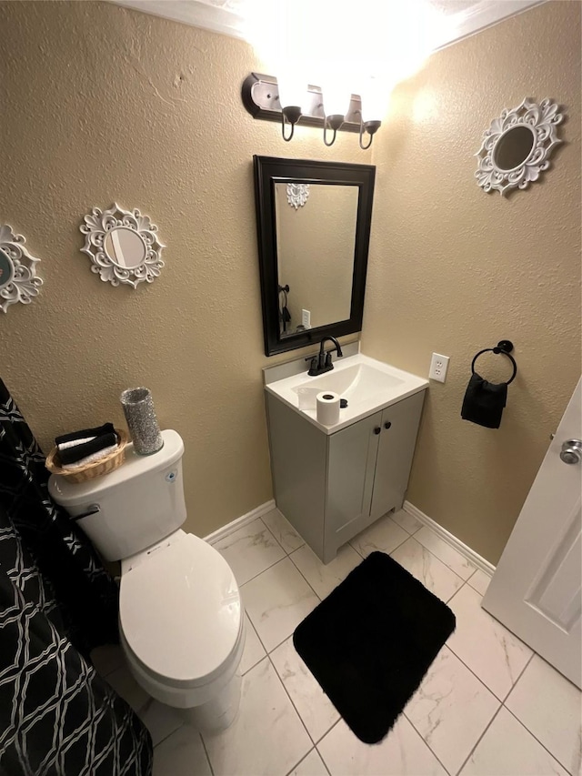 bathroom with baseboards, a textured wall, toilet, marble finish floor, and vanity