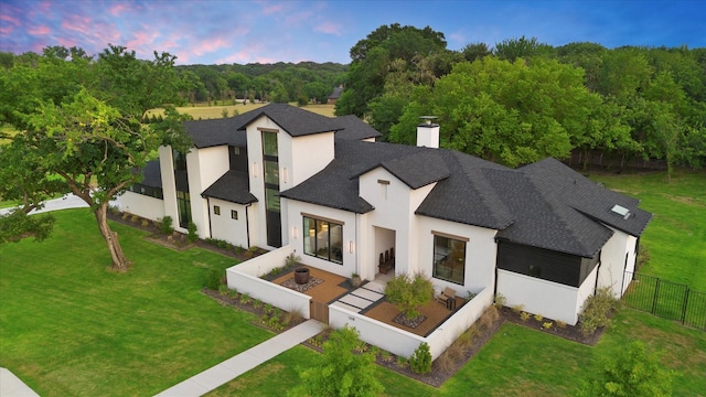 view of front facade featuring a fenced backyard, roof with shingles, stucco siding, a front lawn, and a chimney