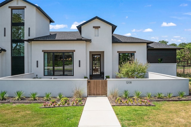 view of front of property with a fenced front yard, roof with shingles, a gate, stucco siding, and a front lawn