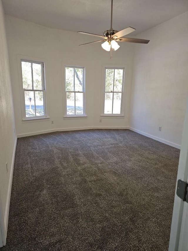 empty room featuring dark colored carpet, ceiling fan, and baseboards