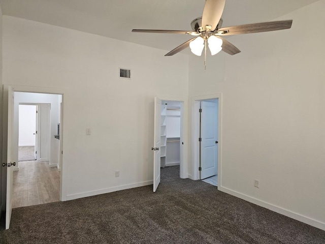 unfurnished bedroom featuring a towering ceiling, baseboards, visible vents, carpet, and a walk in closet