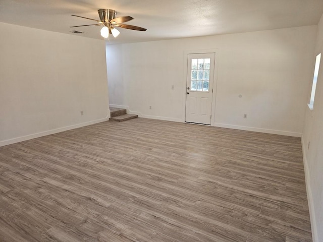 unfurnished room with ceiling fan, stairs, baseboards, and wood finished floors