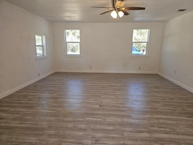 unfurnished room with a ceiling fan, visible vents, dark wood finished floors, and baseboards