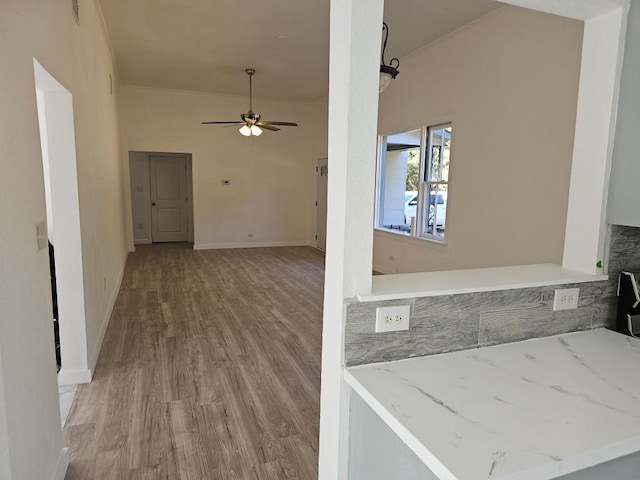 interior space with ceiling fan, baseboards, light stone counters, and wood finished floors