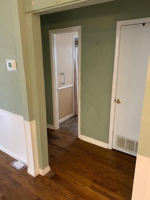 hallway with dark wood-style flooring, visible vents, and baseboards