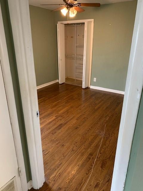 unfurnished bedroom with ceiling fan, wood finished floors, visible vents, baseboards, and a closet