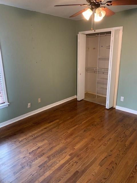 unfurnished bedroom with a ceiling fan, baseboards, dark wood finished floors, and a closet