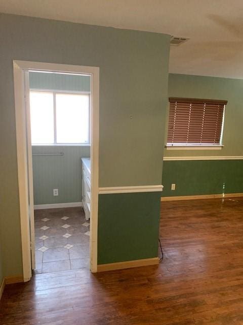 empty room with wood finished floors, visible vents, and baseboards