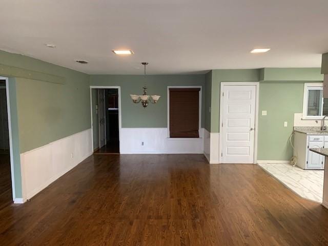 unfurnished room with an inviting chandelier, wood finished floors, and wainscoting