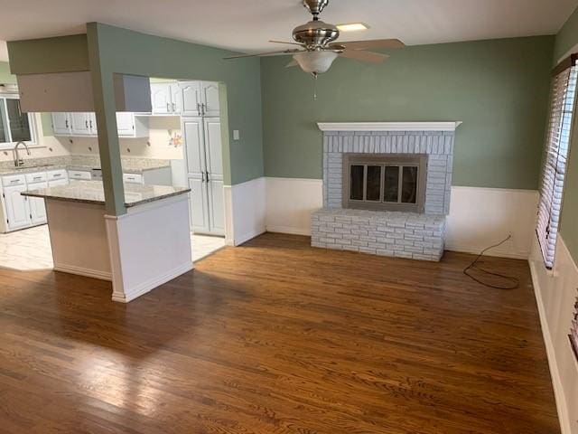 unfurnished living room with a sink, a fireplace, a ceiling fan, and wood finished floors