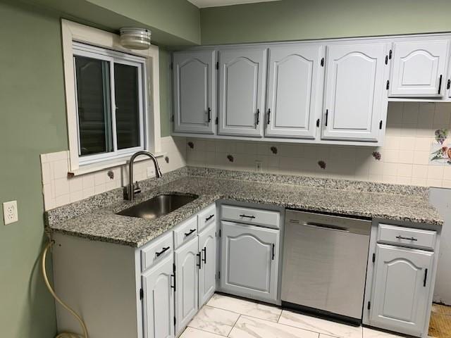 kitchen with stone counters, a sink, white cabinets, stainless steel dishwasher, and decorative backsplash