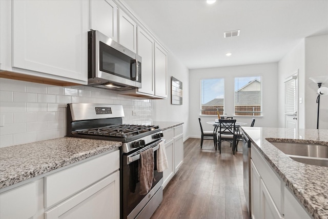 kitchen featuring dark wood-style floors, stainless steel appliances, tasteful backsplash, visible vents, and white cabinetry