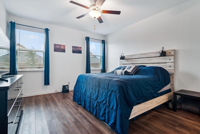 bedroom featuring dark wood-type flooring, multiple windows, baseboards, and a ceiling fan