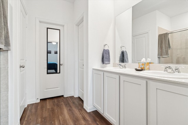 full bathroom featuring double vanity, a sink, a tile shower, and wood finished floors