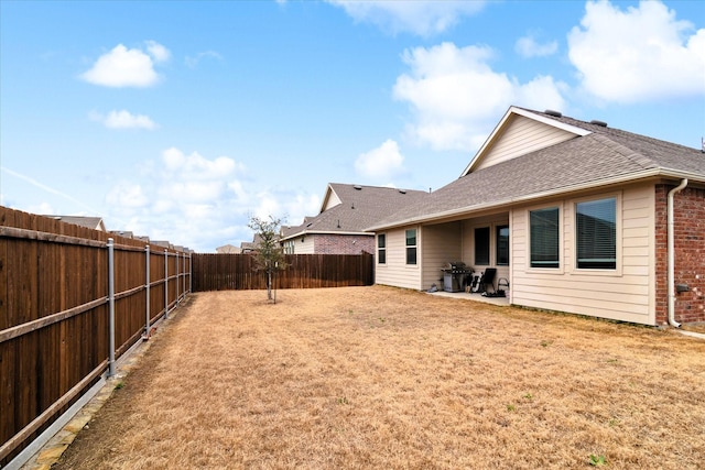 rear view of house with a patio, a fenced backyard, brick siding, roof with shingles, and a lawn