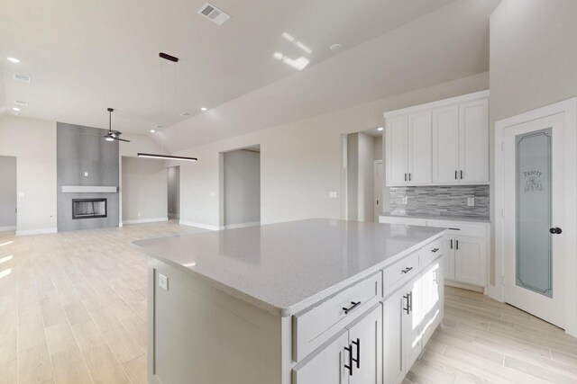 kitchen with visible vents, a kitchen island, lofted ceiling, decorative backsplash, and light wood-style flooring