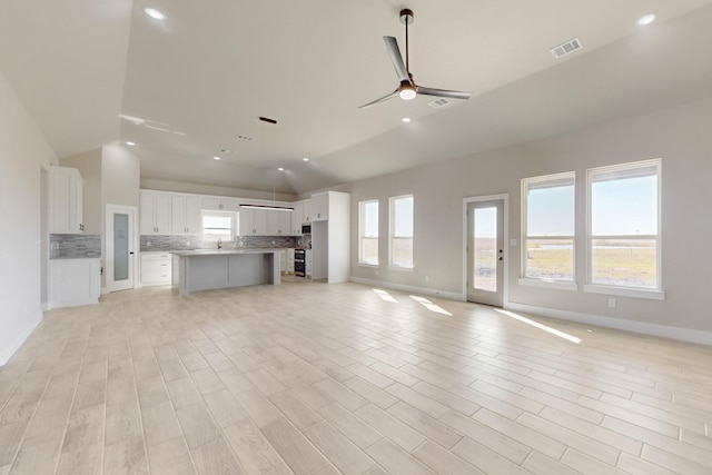 unfurnished living room with lofted ceiling, a ceiling fan, visible vents, and light wood finished floors