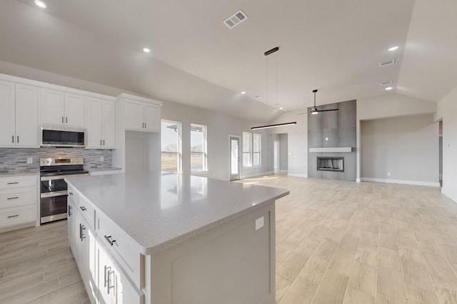 kitchen featuring lofted ceiling, a large fireplace, visible vents, and stainless steel appliances