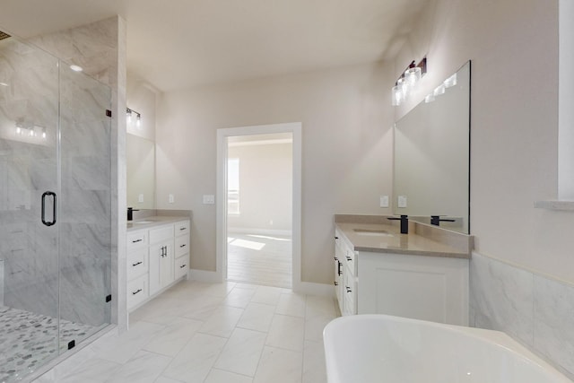 full bathroom with a sink, a marble finish shower, a freestanding bath, and two vanities