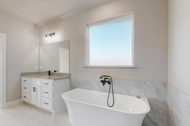 bathroom featuring marble finish floor, a freestanding bath, vanity, and tile walls