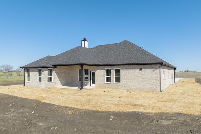 back of house featuring a chimney, brick siding, and a shingled roof