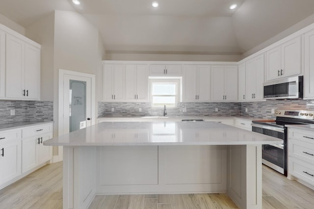 kitchen featuring a kitchen island, stainless steel appliances, white cabinets, decorative backsplash, and vaulted ceiling