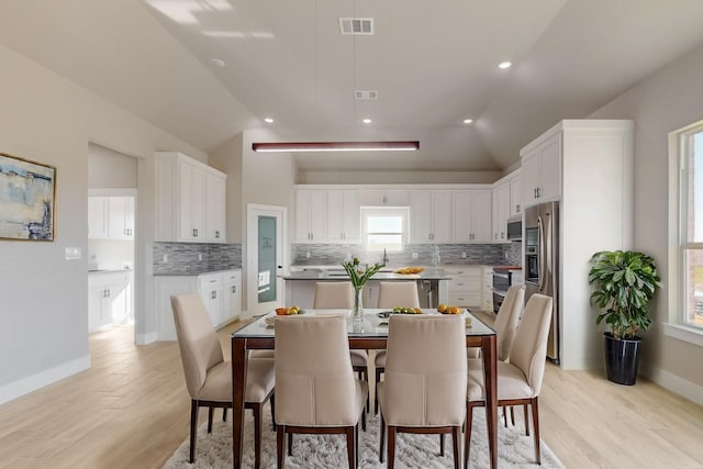 dining room featuring lofted ceiling, baseboards, visible vents, and light wood finished floors